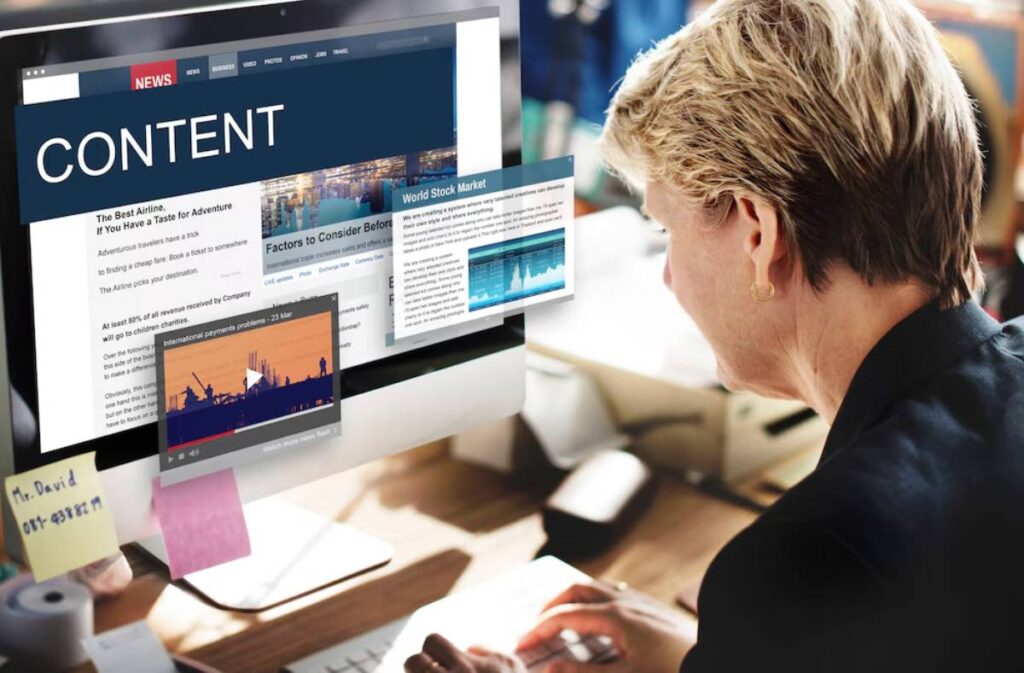 Woman at a desk reads a digital content news website on her computer monitor.