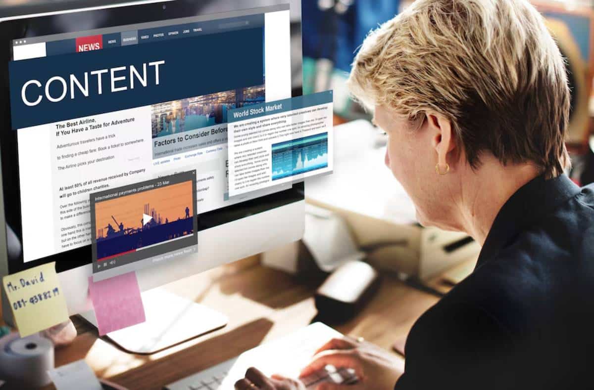Woman at a desk reads a digital content news website on her computer monitor.