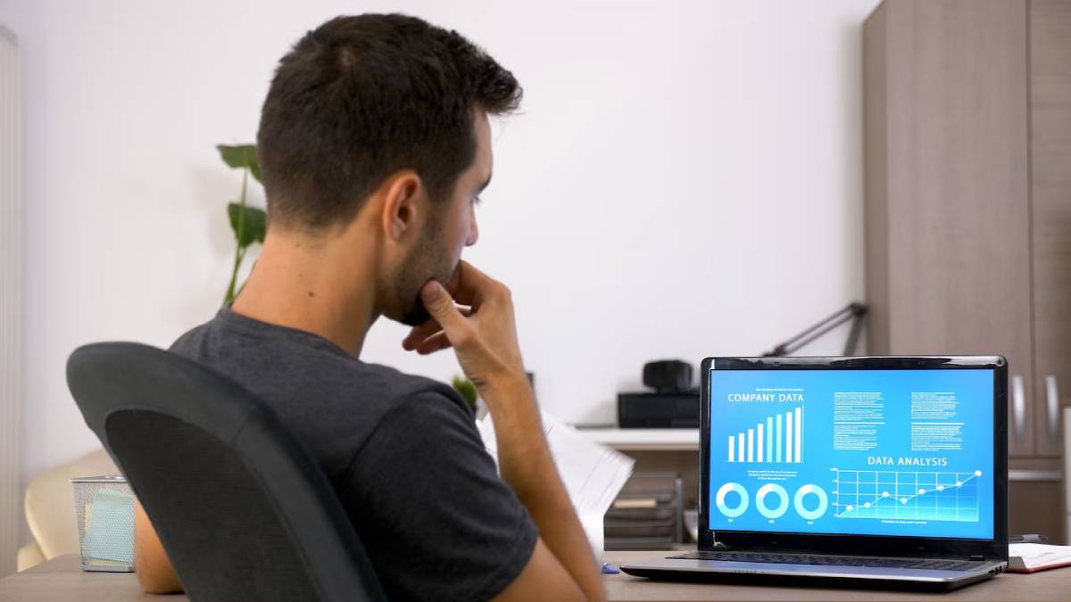 A Man analyzing data charts on a laptop screen in a home office.