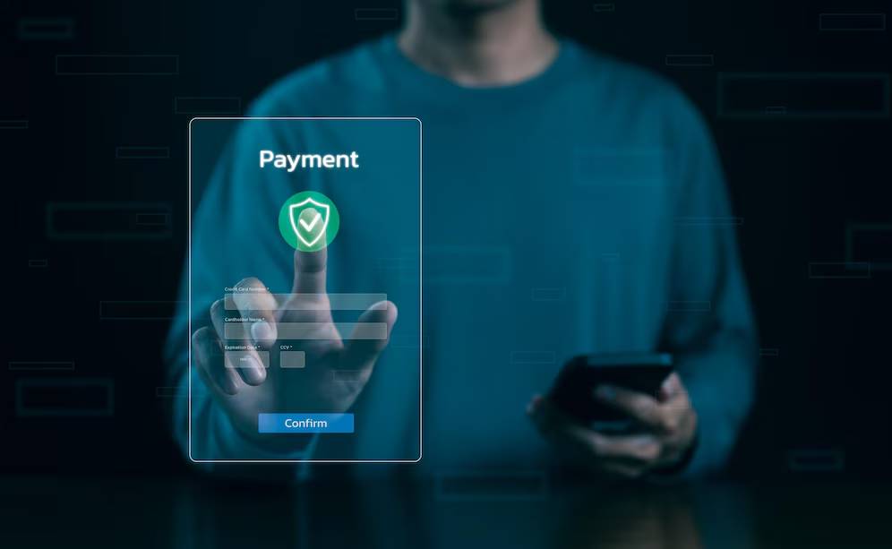 Person in blue shirt using a futuristic digital payment interface on a transparent screen while holding a smartphone.