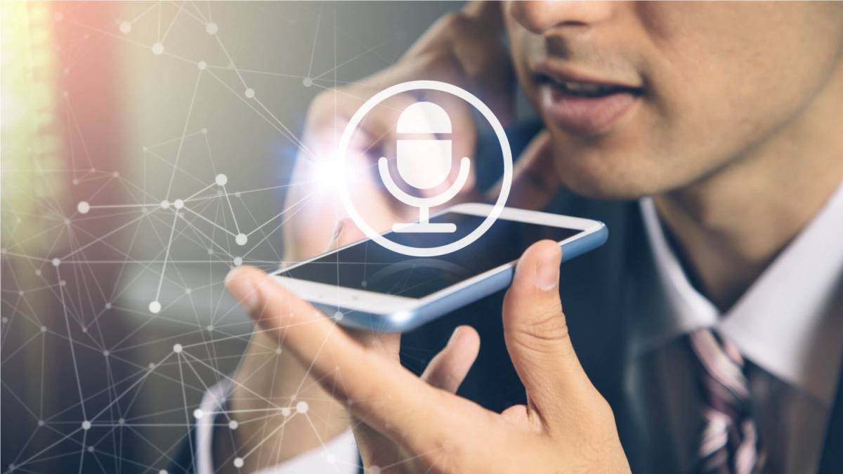 A man in a suit using a smartphone with a voice command icon, symbolizing modern technology communication.