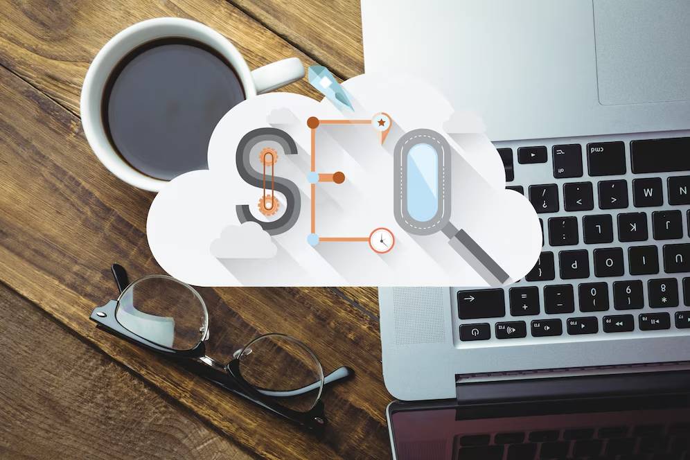 Laptop with cloud computing and SEO icons, coffee cup, and glasses on a wooden table.