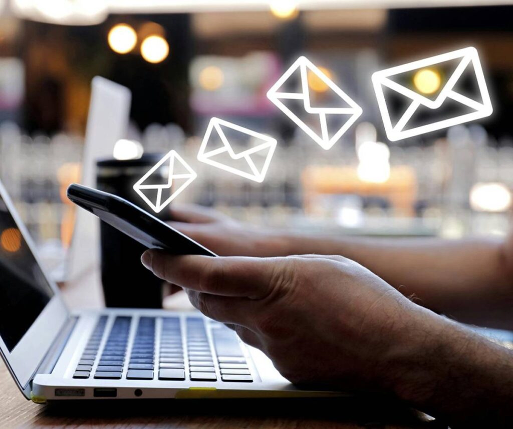 Man using smartphone and laptop at a cafe, with graphic icons of emails floating above the devices.