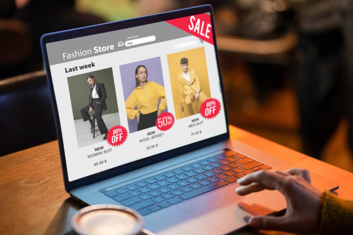Person shopping online viewing a laptop screen displaying a fashion sale with discounted clothing items.