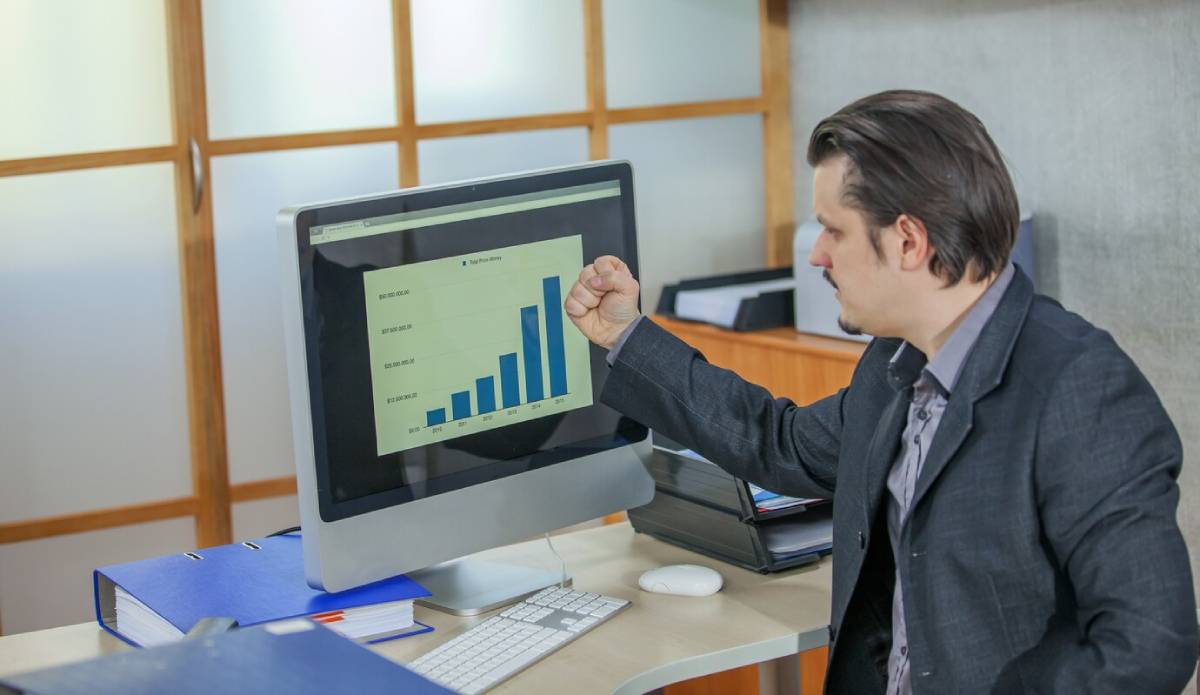 Man in suit analyzing bar graph data on a computer screen in an office setting.