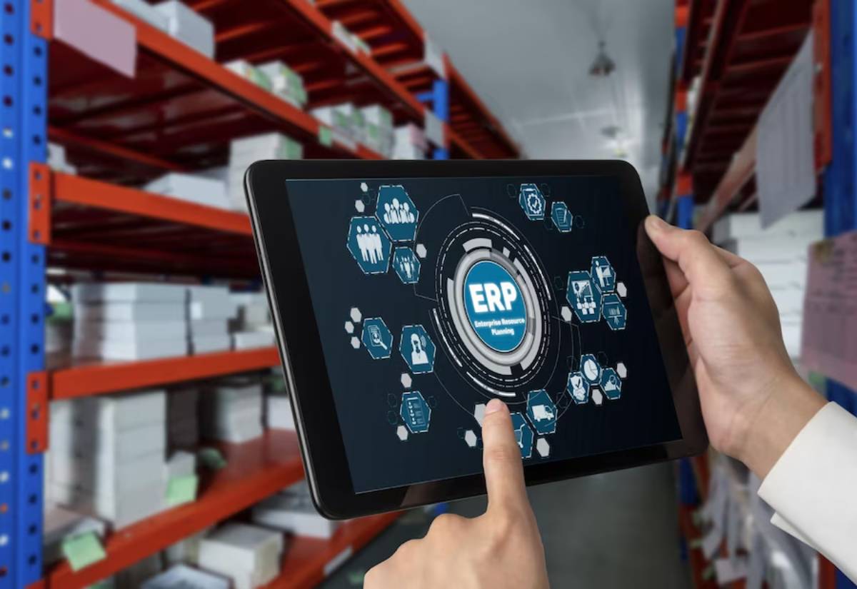 Person in a warehouse using a tablet displaying an ERP (Enterprise Resource Planning) system interface.
