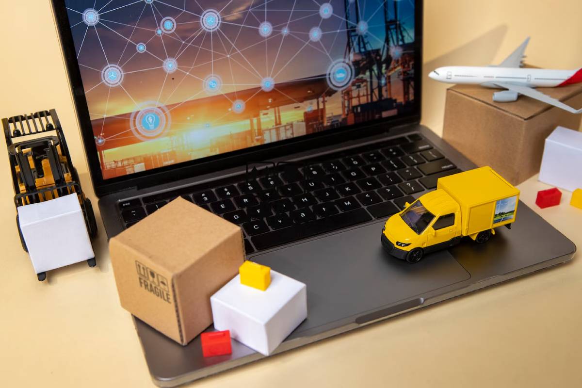Miniature delivery truck and airplane on laptop displaying logistics network, with packages and a forklift nearby on a desk.