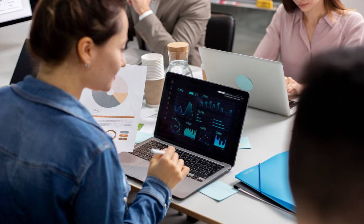 Three professionals analyze data charts on laptops during a business meeting.