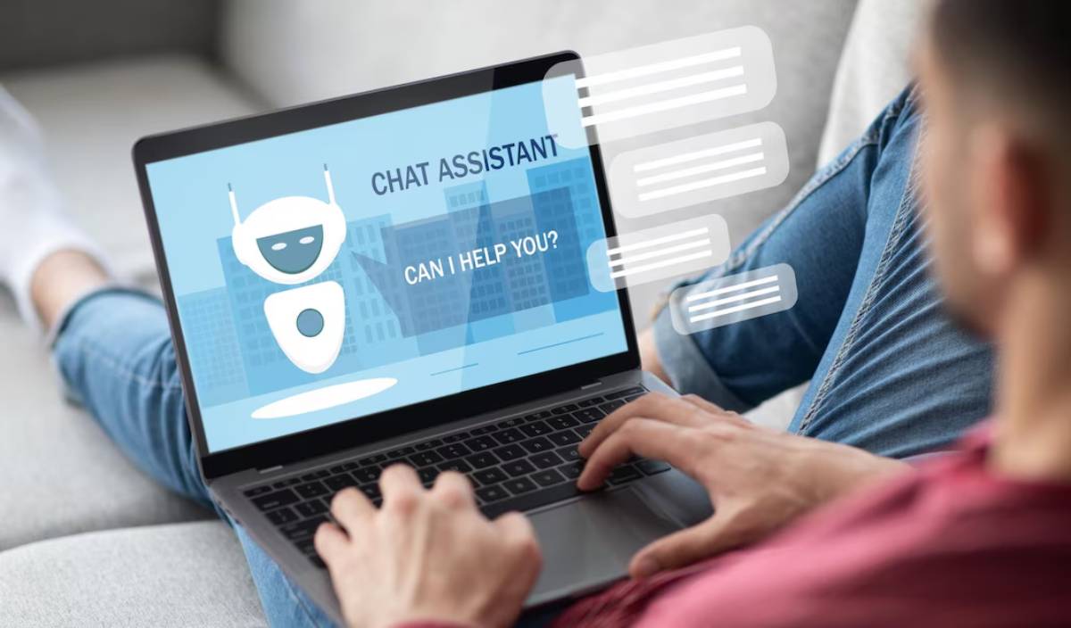 Person using laptop with a chatbot assistant on the screen asking, Can I help you?