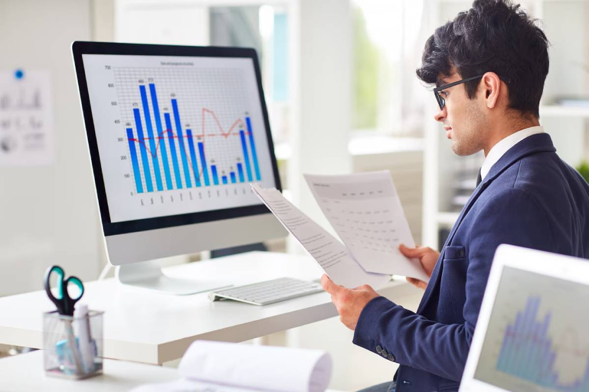 Businessman analyzing financial graphs on a computer screen in a modern office.
