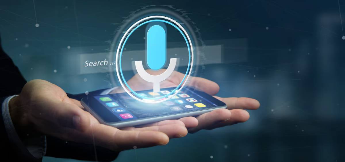 A person using a smartphone with a digital voice assistant icon displayed above it, indicating voice search technology.
