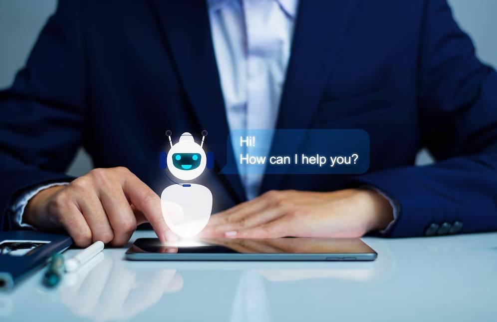 A businessman interacts with a virtual assistant robot on a tablet, displaying the message Hi! How can I help you?
