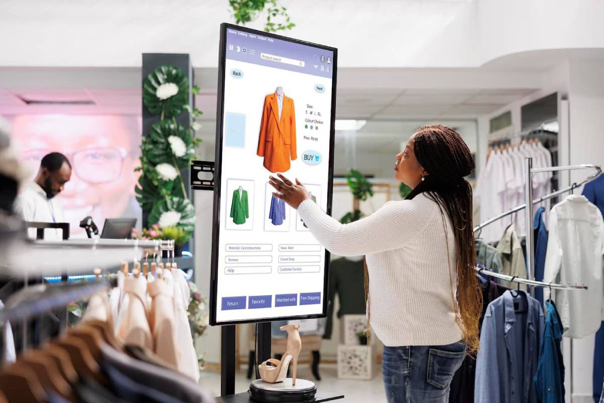 A woman using a large digital screen to browse clothing options in a modern retail store.